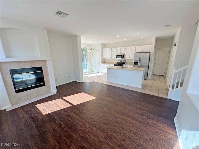 kitchen with stainless steel appliances, light wood-style flooring, a sink, visible vents, and a tile fireplace