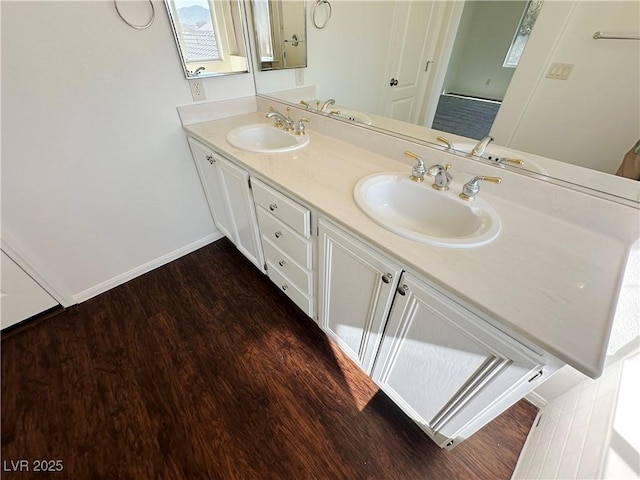 bathroom with baseboards, wood finished floors, a sink, and double vanity