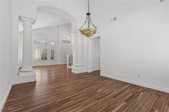 283 Grand Olympia Dr, Henderson, NV 89012 - unfurnished dining area featuring a towering ceiling, baseboards, dark wood-type flooring, and decorative columns