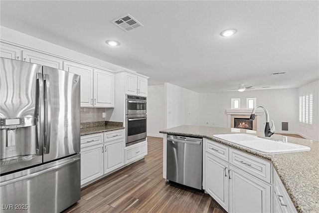 283 Grand Olympia Dr, Henderson, NV 89012 - kitchen featuring appliances with stainless steel finishes, a sink, ceiling fan, a warm lit fireplace, and white cabinets