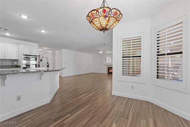 283 Grand Olympia Dr, Henderson, NV 89012 - kitchen with a breakfast bar area, baseboards, a warm lit fireplace, dark wood-type flooring, and recessed lighting