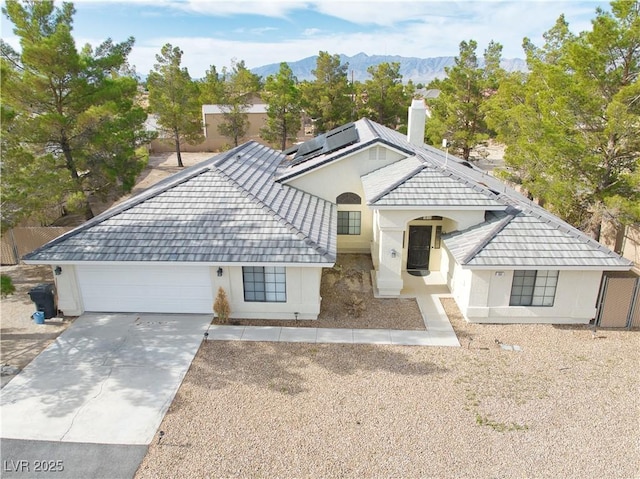 151 Hornet St, Pahrump, NV 89048 - view of front of property with a garage, driveway, solar panels, a mountain view, and a chimney