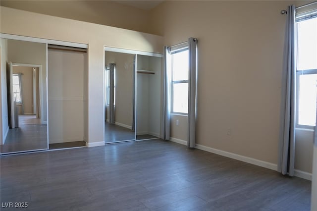 unfurnished bedroom with two closets, dark wood finished floors, baseboards, and multiple windows