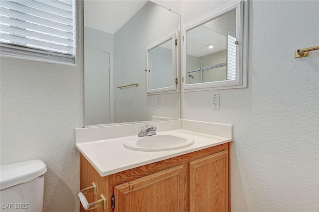 bathroom featuring toilet, a textured wall, and vanity