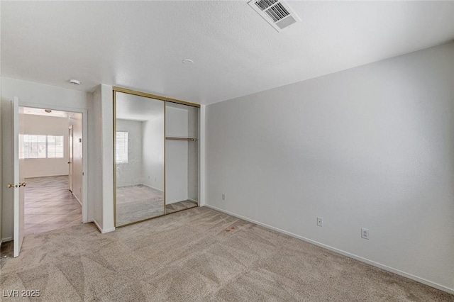 unfurnished bedroom with baseboards, visible vents, a closet, and light colored carpet