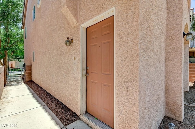 view of exterior entry featuring stucco siding and fence