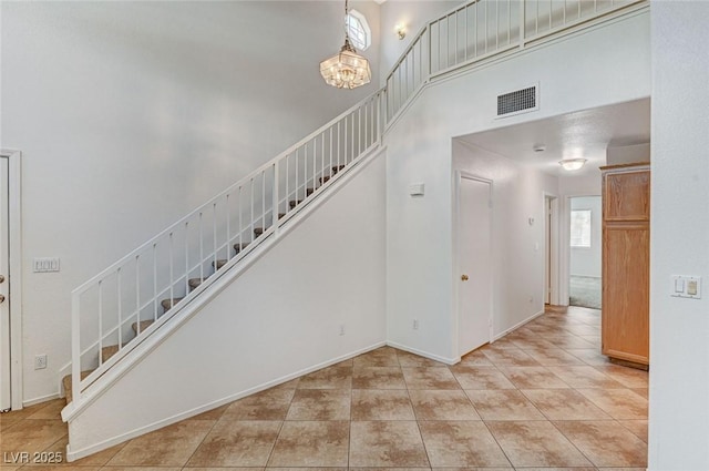 stairs featuring tile patterned flooring, a chandelier, visible vents, and a towering ceiling