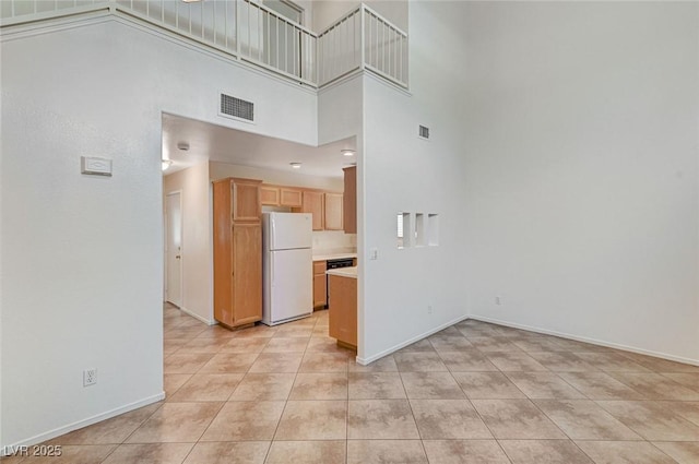 empty room with baseboards, visible vents, a towering ceiling, and light tile patterned floors