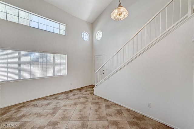 unfurnished living room featuring baseboards, a towering ceiling, a chandelier, tile patterned flooring, and stairs