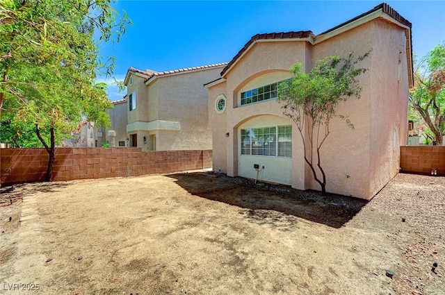 rear view of house featuring stucco siding, a tiled roof, and fence
