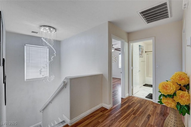hallway with baseboards, wood finished floors, visible vents, and an upstairs landing