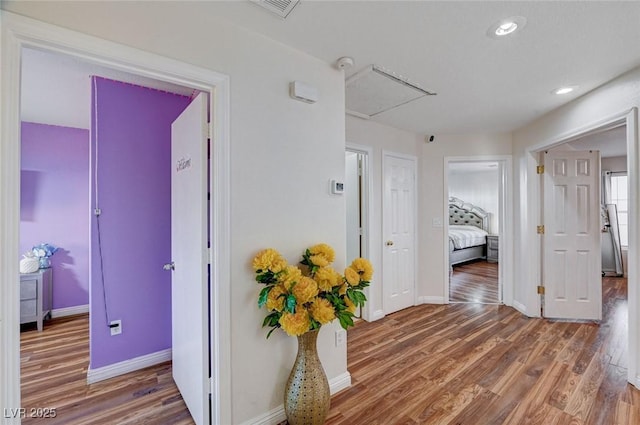 corridor with attic access, visible vents, baseboards, recessed lighting, and wood finished floors