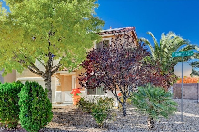 view of property hidden behind natural elements with stucco siding, roof mounted solar panels, and a tile roof