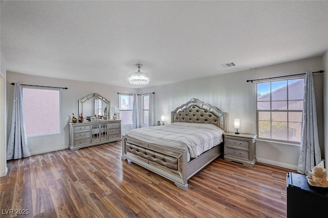 bedroom with wood finished floors, visible vents, baseboards, and an inviting chandelier