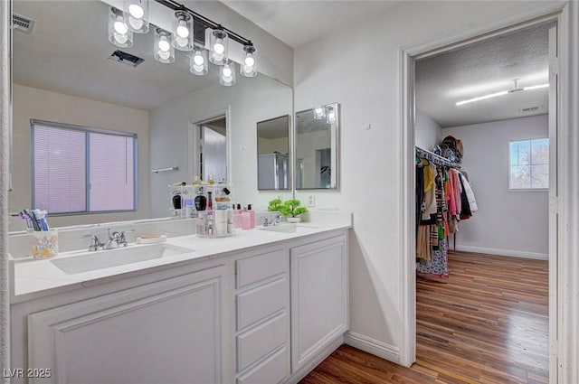 bathroom with a sink, double vanity, baseboards, visible vents, and wood finished floors