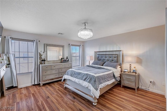 bedroom with wood finished floors, visible vents, baseboards, and a notable chandelier