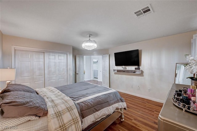 bedroom with wood finished floors, visible vents, a closet, baseboards, and a notable chandelier