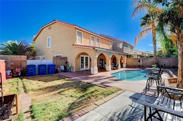 back of property with a fenced backyard, a tiled roof, stucco siding, french doors, and a patio