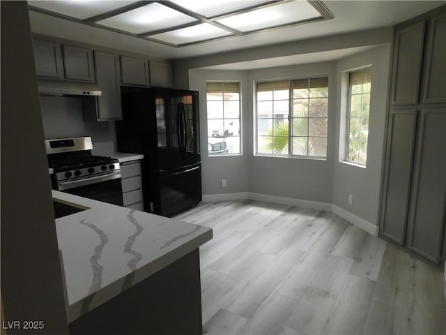 kitchen featuring light stone counters, under cabinet range hood, freestanding refrigerator, gas stove, and baseboards