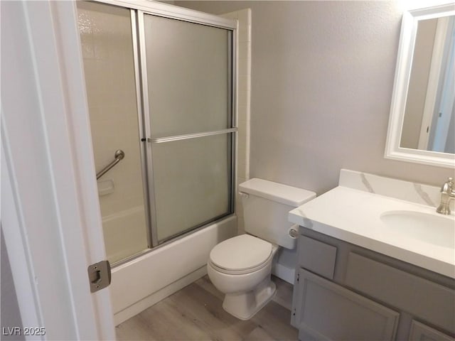 full bath with wood finished floors, vanity, shower / bath combination with glass door, and toilet