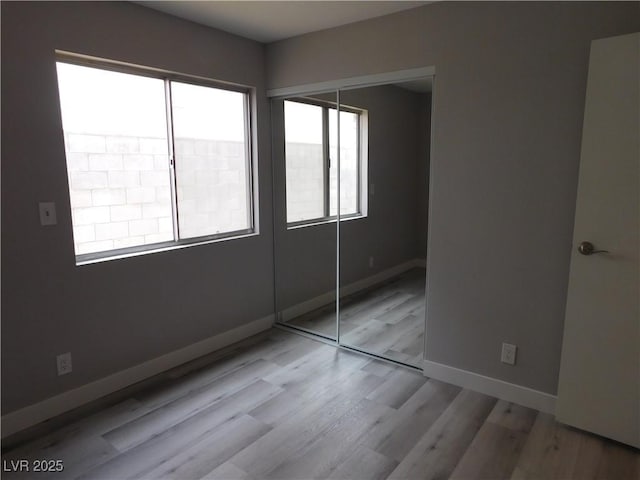 unfurnished bedroom featuring baseboards, wood finished floors, and a closet