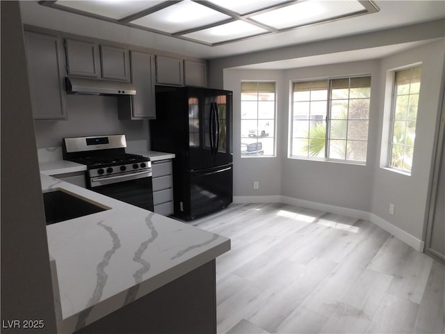 kitchen with a sink, baseboards, freestanding refrigerator, under cabinet range hood, and stainless steel gas range oven