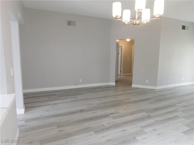 spare room featuring baseboards, light wood-style flooring, visible vents, and a chandelier