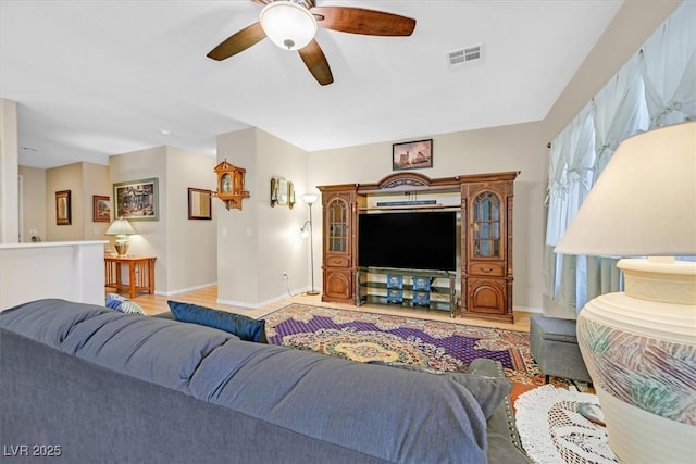 living room with light wood-style floors, visible vents, baseboards, and ceiling fan