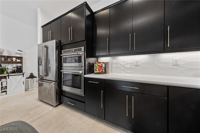 kitchen featuring decorative backsplash, appliances with stainless steel finishes, light countertops, light wood finished floors, and dark cabinets