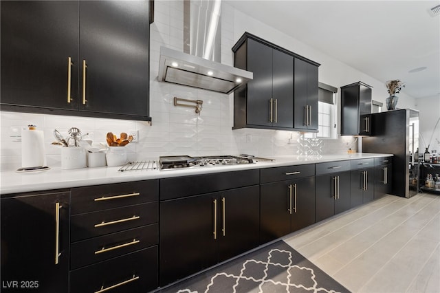 kitchen with wall chimney range hood, light countertops, dark cabinetry, and stainless steel gas stovetop