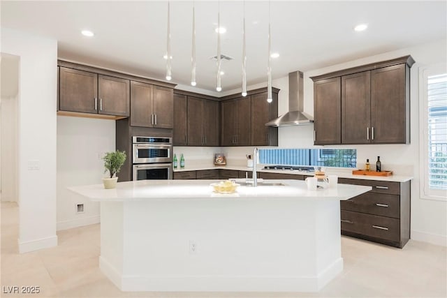 kitchen with wall chimney range hood, appliances with stainless steel finishes, dark brown cabinetry, and a sink