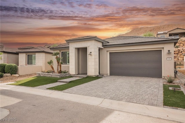 prairie-style house with stucco siding, decorative driveway, and a garage