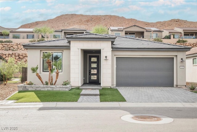 prairie-style home with a mountain view, fence, a garage, stucco siding, and decorative driveway