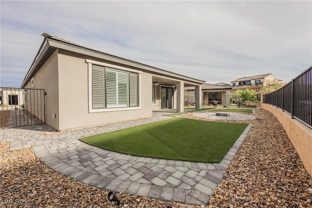 rear view of property with a patio area, a lawn, a fenced backyard, a fire pit, and stucco siding