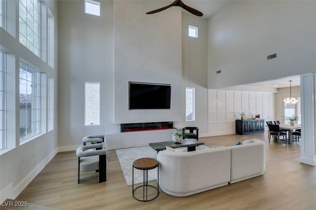 living area featuring a wealth of natural light, a towering ceiling, visible vents, and ceiling fan with notable chandelier