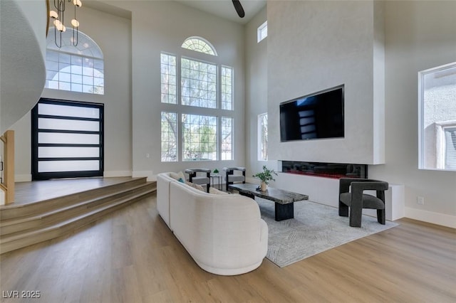 living area with baseboards, wood finished floors, a towering ceiling, and a wealth of natural light