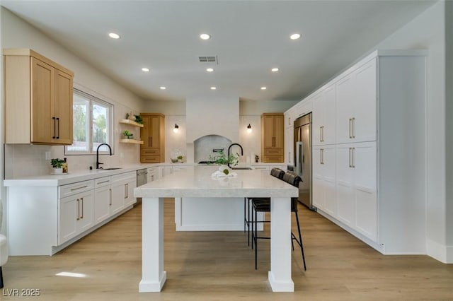kitchen with light countertops, high end fridge, visible vents, a center island with sink, and a kitchen bar
