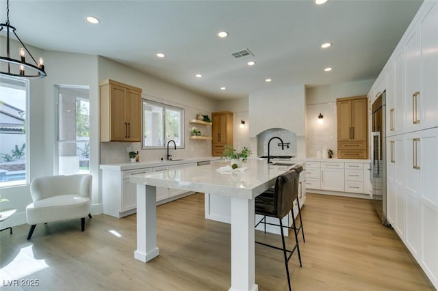 kitchen with light wood finished floors, a kitchen island with sink, a sink, and a kitchen bar