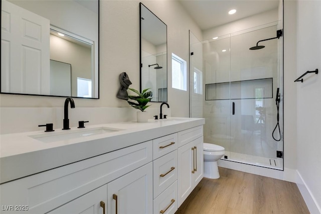 bathroom featuring wood finished floors, a sink, a stall shower, double vanity, and toilet