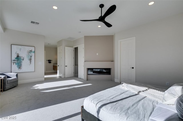 carpeted bedroom with a glass covered fireplace, baseboards, visible vents, and recessed lighting