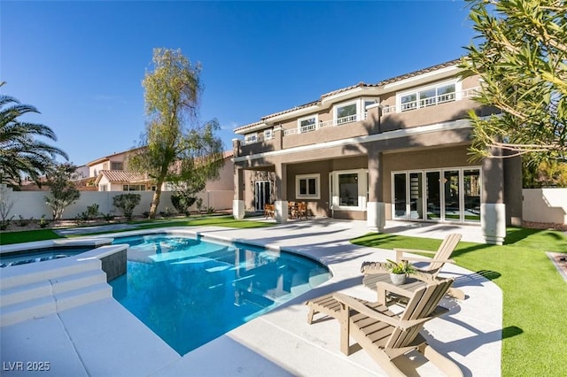 rear view of house with a balcony, fence, a patio, stucco siding, and a pool with connected hot tub
