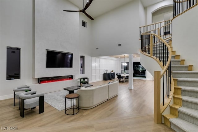 living room featuring stairs, wood finished floors, ceiling fan, a towering ceiling, and baseboards