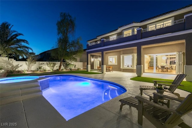 pool at twilight featuring a patio area, a pool with connected hot tub, and fence