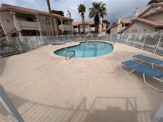 community pool with fence, a hot tub, a patio, and a residential view
