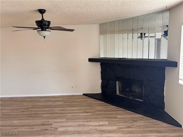 detailed view of wood finished floors, a textured ceiling, ceiling fan, a stone fireplace, and baseboards