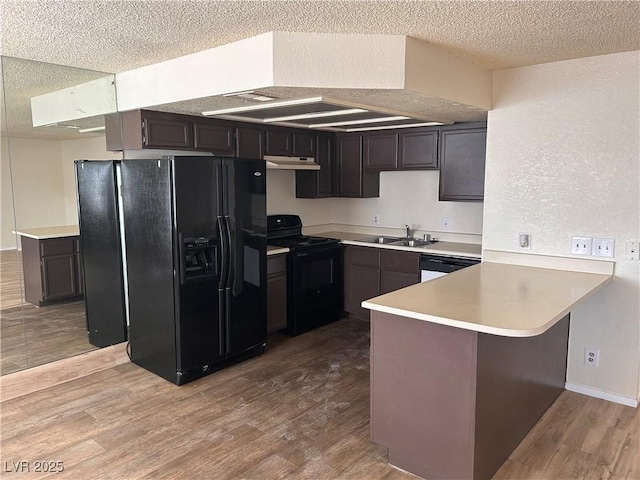 kitchen with black appliances, a sink, a peninsula, light wood finished floors, and under cabinet range hood