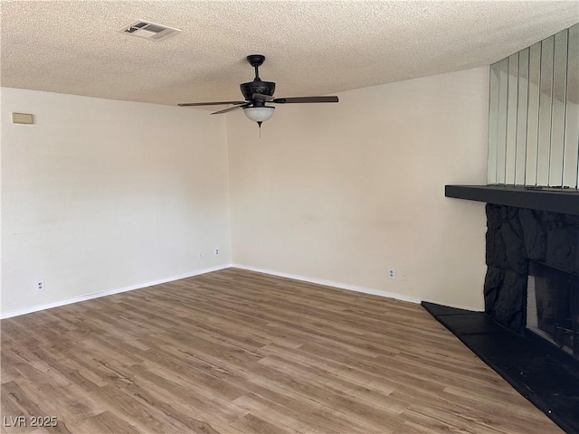 unfurnished living room with ceiling fan, wood finished floors, a textured ceiling, a fireplace, and baseboards