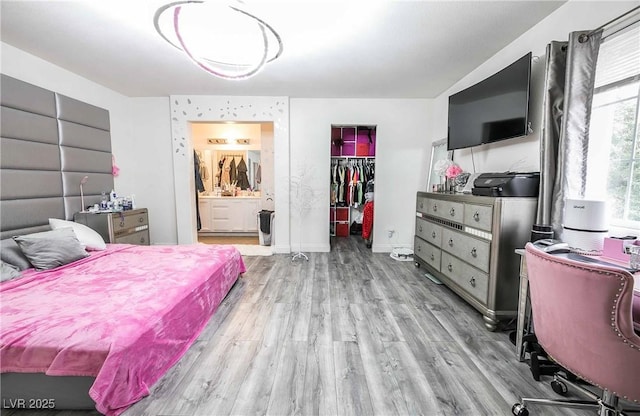 bedroom with ensuite bathroom, baseboards, a spacious closet, wood finished floors, and a closet