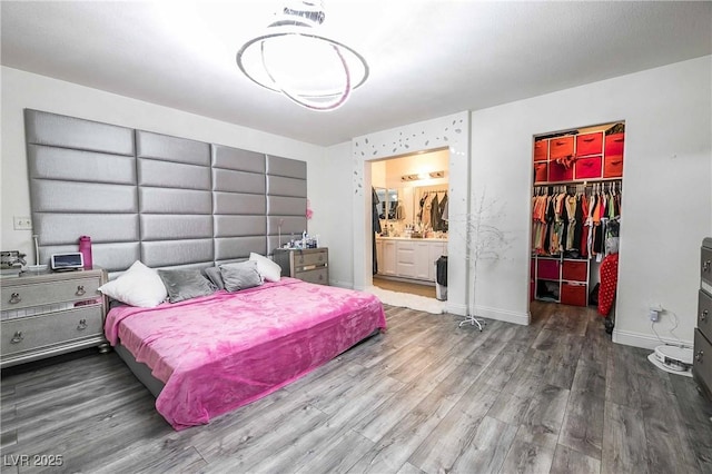 bedroom featuring a spacious closet, wood finished floors, a closet, baseboards, and ensuite bathroom