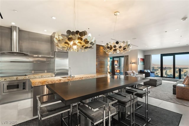 kitchen with a sink, light tile patterned flooring, open floor plan, a notable chandelier, and wall chimney range hood